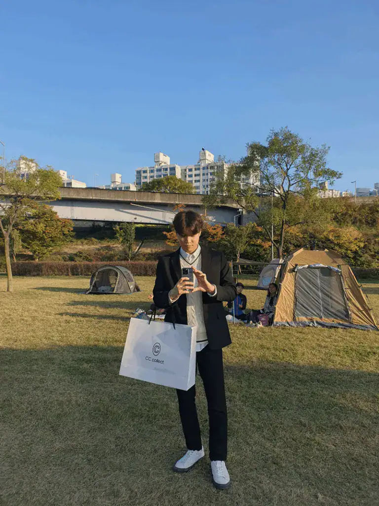 Foto seluruh tubuh Seojun berdiri di atas rumput. Ia mengenakan jaket dan celana hitam dengan sepatu putih.