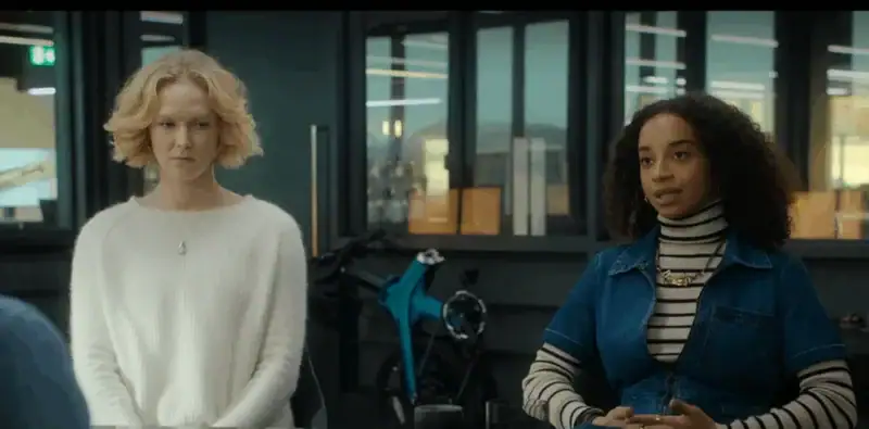 Seorang wanita berambut pirang dan seorang wanita berambut keriting sedang berbicara di dalam ruangan.