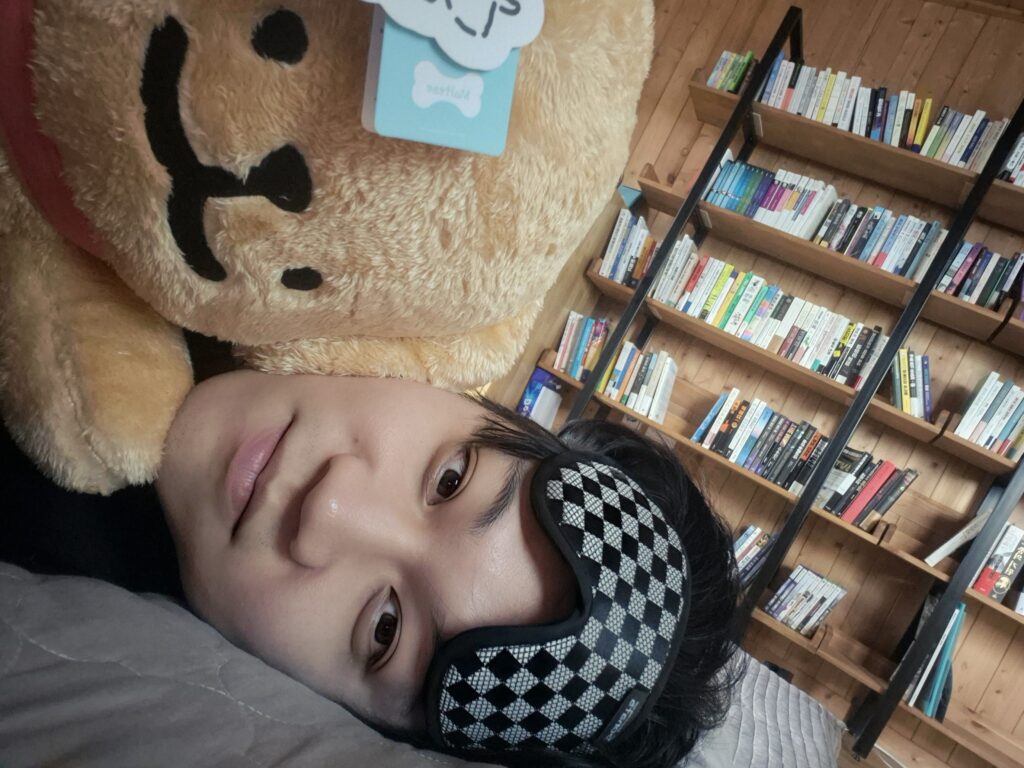 Foto perbandingan ukuran asli seorang pria dewasa setinggi 181cm yang sedang bersantai di tempat tidur sambil memeluk boneka Maltese besar dan bantal guling Retriever