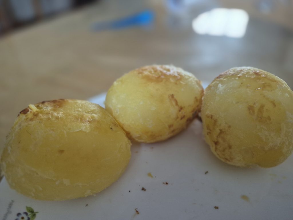 Tiga butir kentang kupas utuh yang dipanggang kuning kecokelatan di atas piring